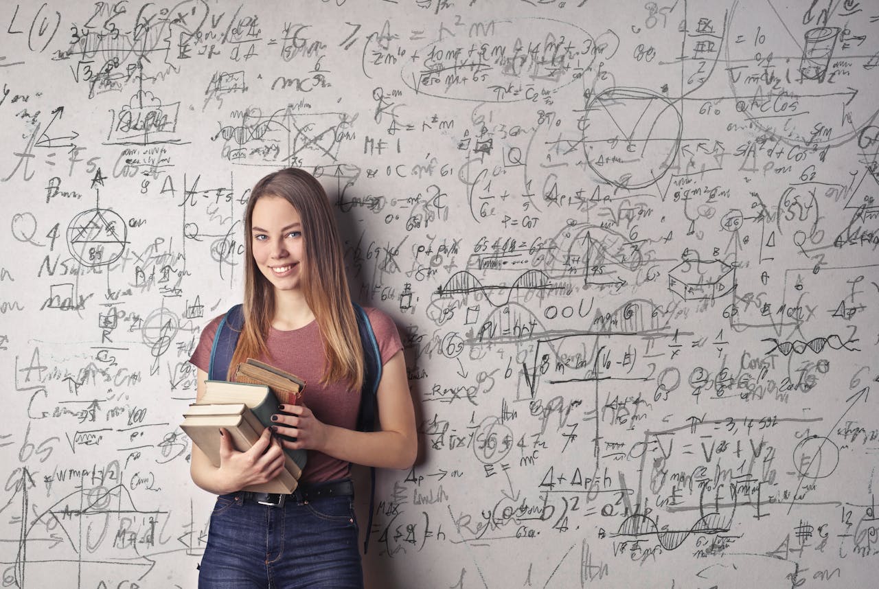 Young woman holding books standing in front of a chalkboard filled with mathematical formulas.